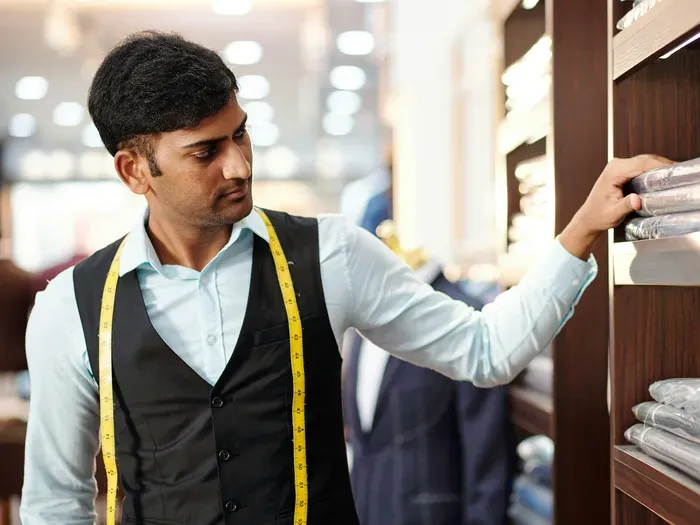 Local tailor with measuring tape selects folded shirts on shelves in a menswear boutique, ready to help